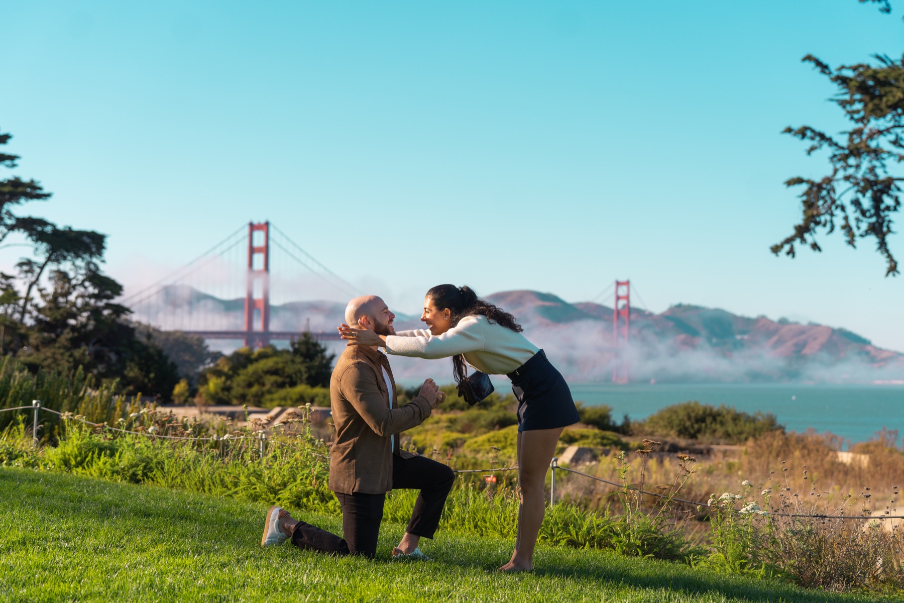 Alex and Abby celebrating after their Golden Gate Bridge — Presidio proposal with the Golden Gate Bridge behind them