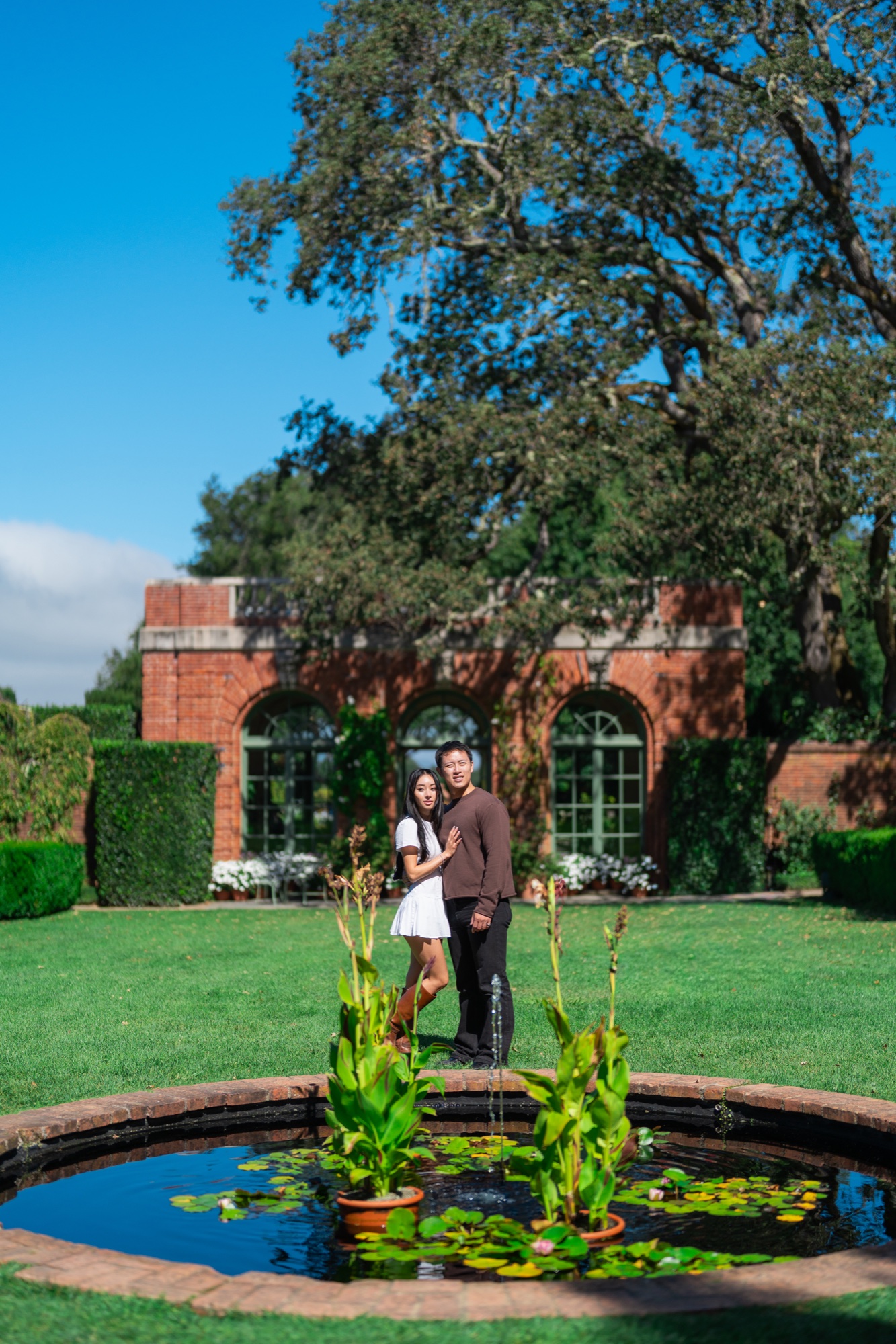 Ernest and Alexandra beside a lily pond with Filoli’s brick garden house behind them